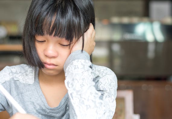 A young girl sits at a table doing homework looking frustrated.