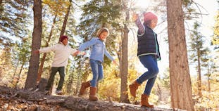 Three children balancing while walking on a log in autumn in the woods.
