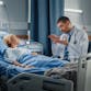 A patient lies in a hospital bed while a doctor explains something to her.