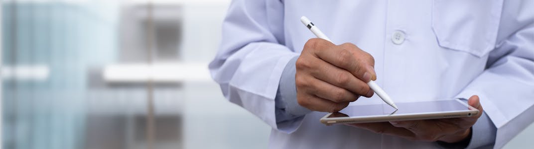 A doctor is shown from the shoulders to the waist holding a tablet with a pen.