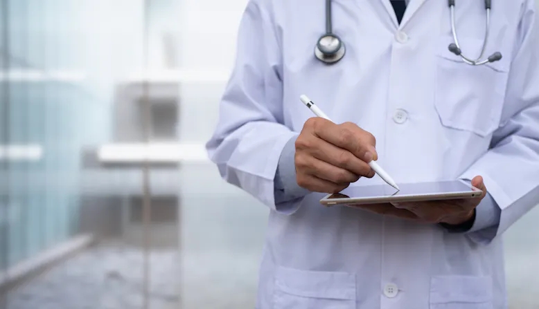 A doctor is shown from the shoulders to the waist holding a tablet with a pen.