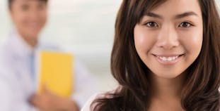 A teen smiles for a camera while the doctor sands behind her.