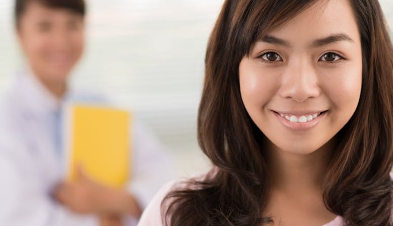 A teen smiles for a camera while the doctor sands behind her.
