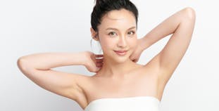 A woman in a strapless white top with her arms up, hands resting behind her neck.