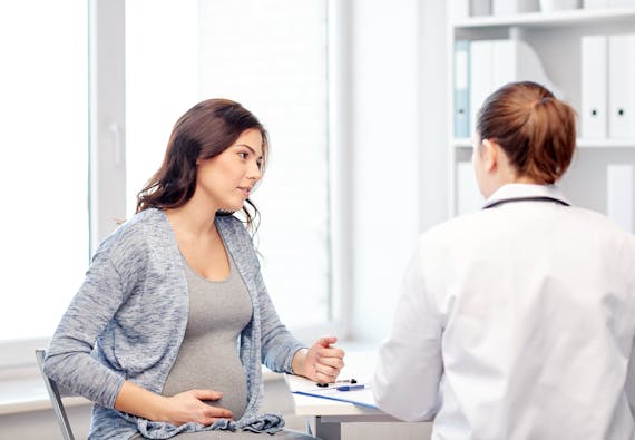 A pregnant woman touches her stomach while conversing with a doctor.