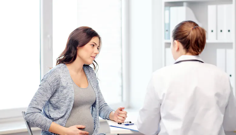 A pregnant woman touches her stomach while conversing with a doctor.