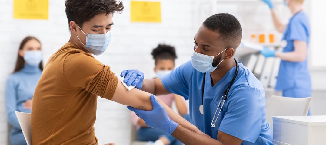 A young man gets prepped for a vaccine by a health care worker.