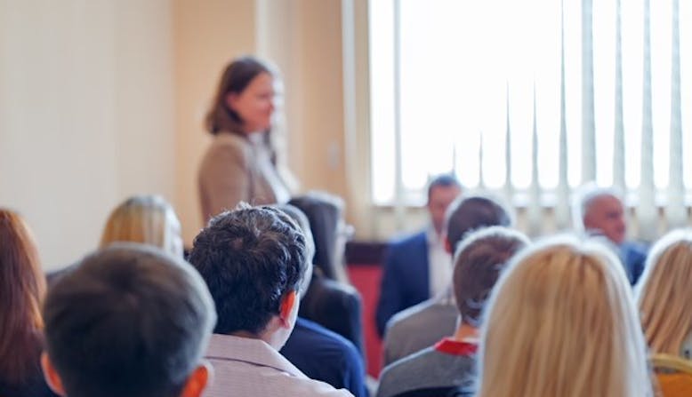 An audience listening to a panel discussion in a brightly lit room.