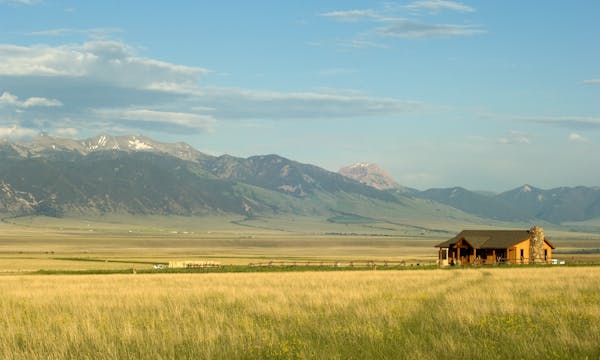 A house in the distance surrounded by a field with mountains in the distance.