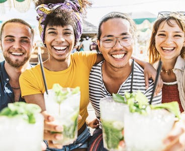 A multiracial group of friends smiling at the camera and toasting with their mojitos.
