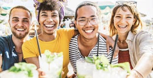 A multiracial group of friends smiling at the camera and toasting with their mojitos.