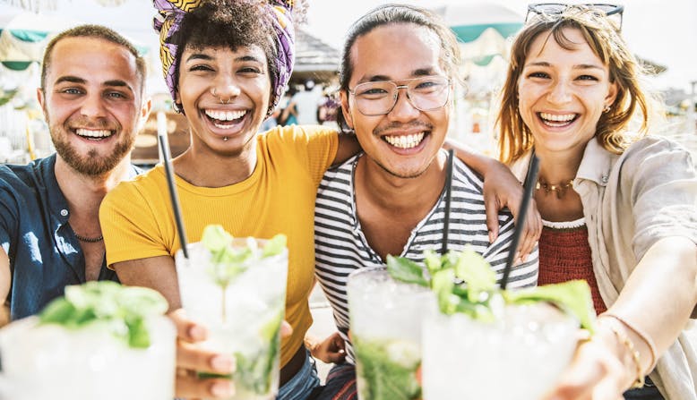 A multiracial group of friends smiling at the camera and toasting with their mojitos.