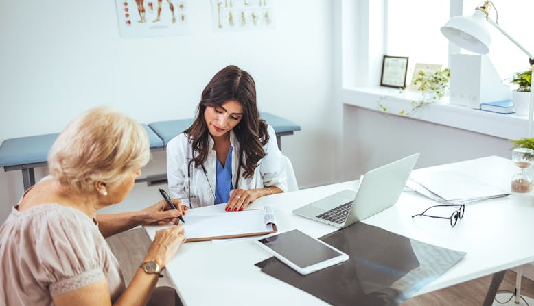 A Hispanic woman doctor reviews a clipboard with an elderly woman patient.