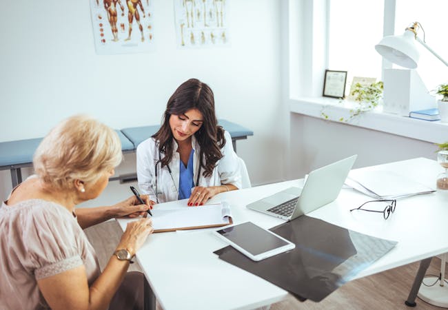 A Hispanic woman doctor reviews a clipboard with an elderly woman patient.
