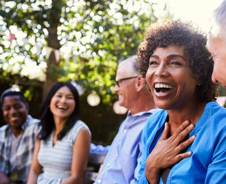 A group of people converse and laugh outside.