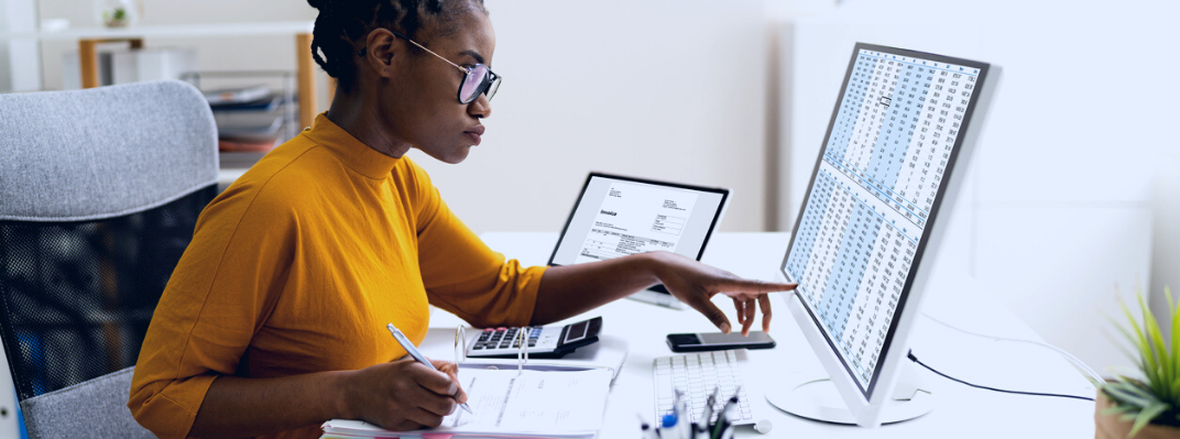 A woman sits at a desk calculating numbers from a spreadsheet.