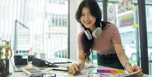 Smiling female creative designer sitting in modern workplace and working with laptop computer.