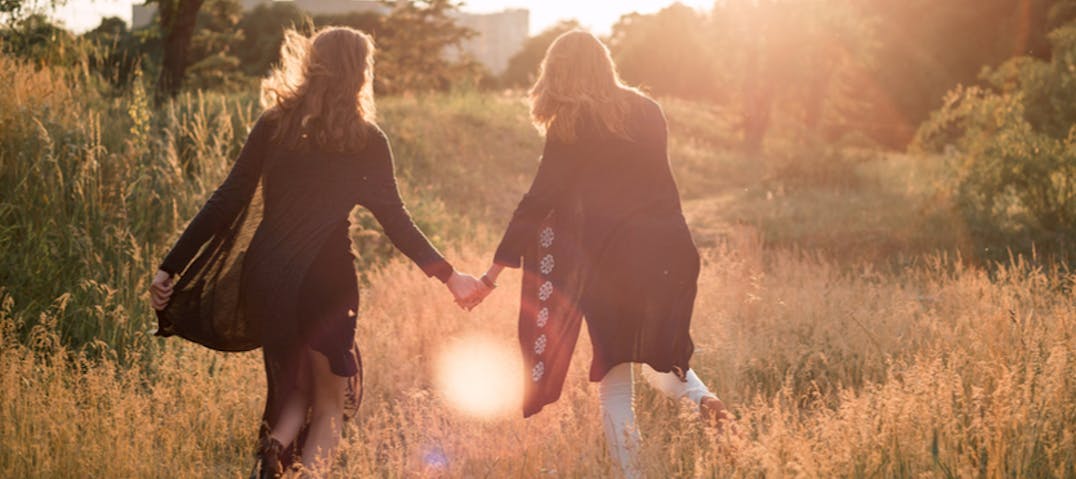 Two women hold hands while walking through a meadow.