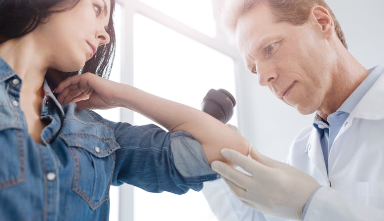 Photo of a dermatologist inspecting a patient's skin on her arm.