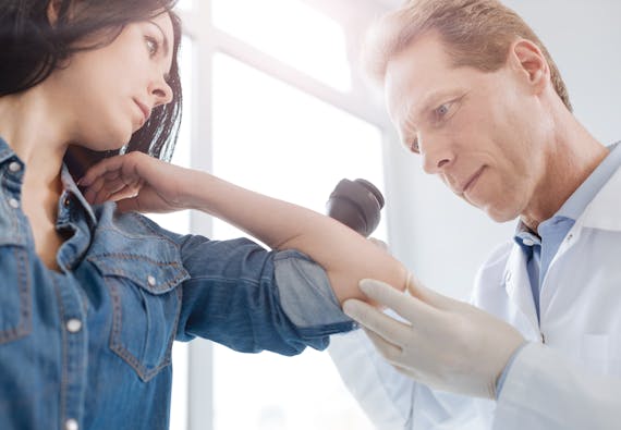 Photo of a dermatologist inspecting a patient's skin on her arm.