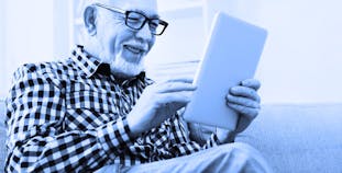 An older man smiles while looking at a tablet. 