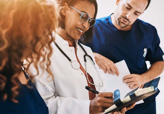 Three health care professionals interact and look over a patient chart.