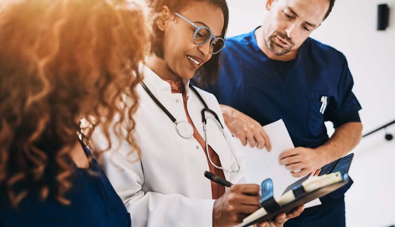 Three health care professionals interact and look over a patient chart.