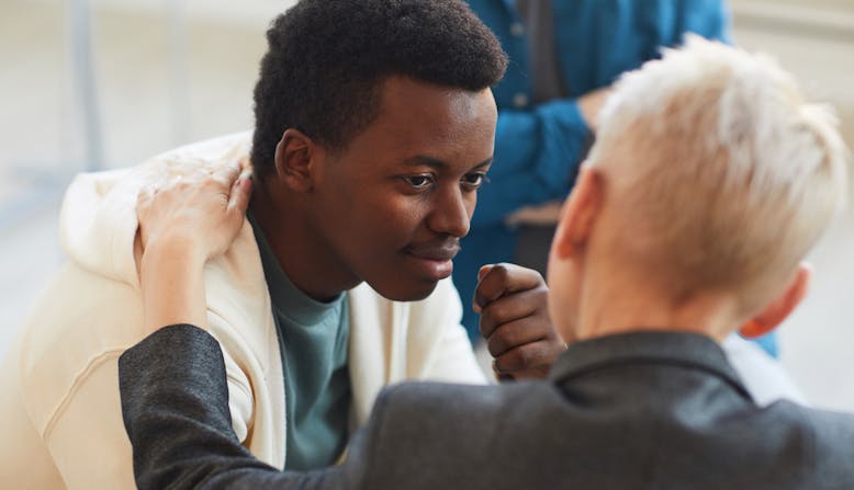A woman provides emotional support to a man in a group setting.