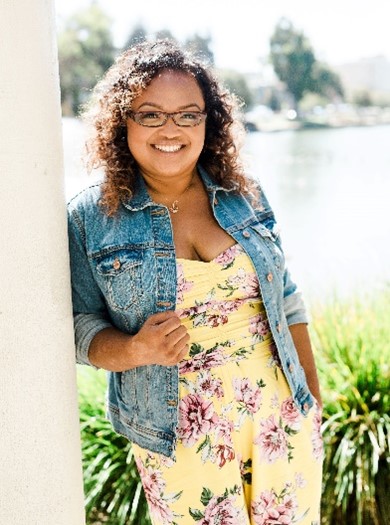 Brenda Kong in a floral jumpsuit and jean jacket, smiling and leaning against a column outside.