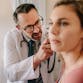 A doctor inspects a female patient's ear in a medical exam room.