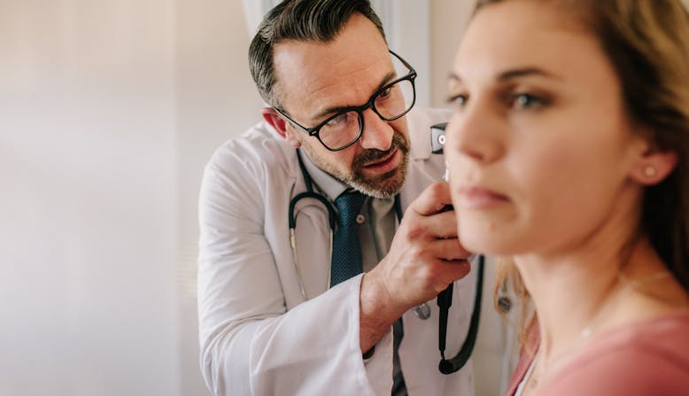 A doctor inspects a female patient's ear in a medical exam room.