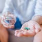 A close-up photo of a person holding pills in one hand and a glass of water in the other hand.