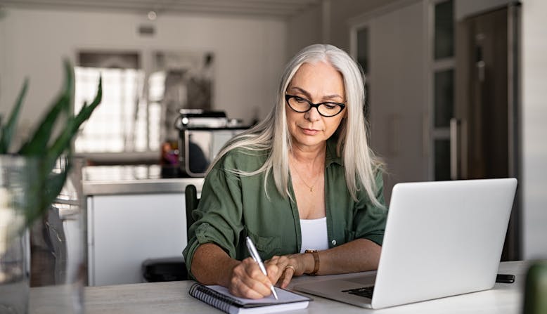 A woman takes notes next to her laptop while sitting in her home.