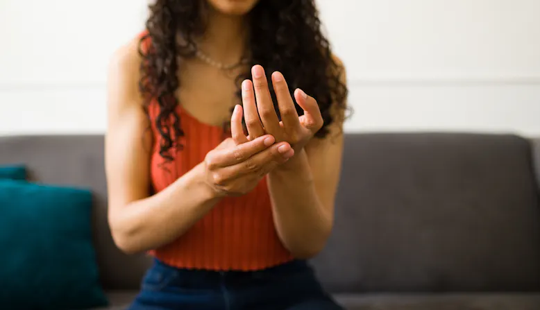 A woman sits on a couch and holds her hand in pain.