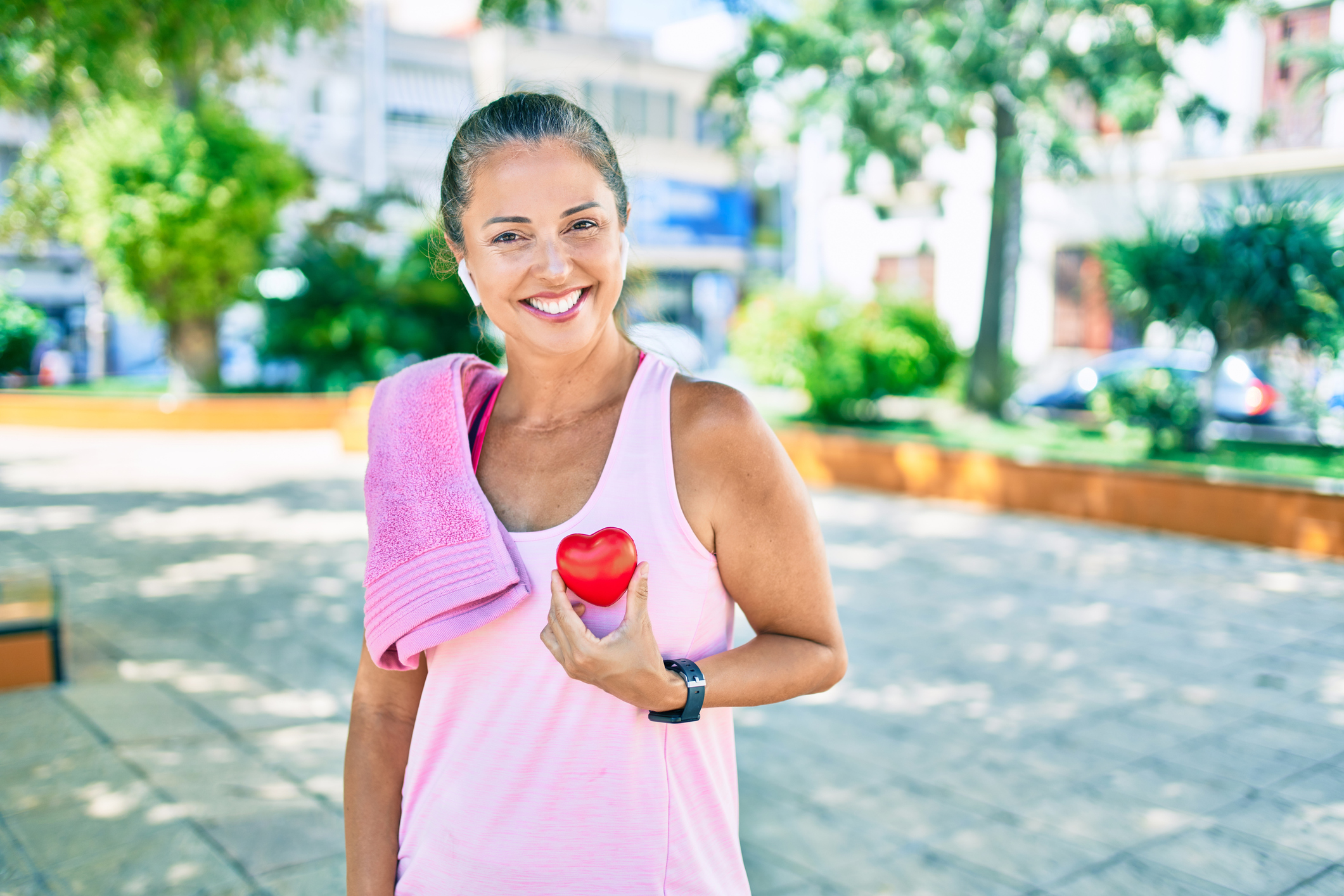 Heart health concept. A woman in workout gear holds a plastic heart up to her chest.