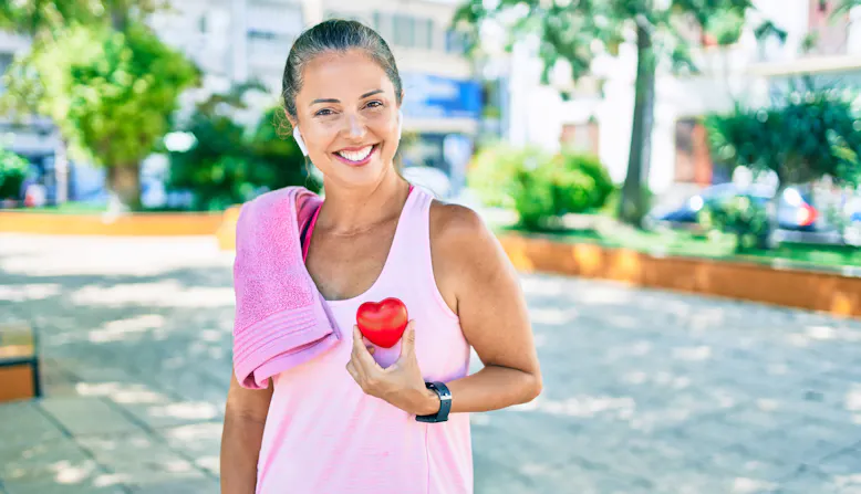 Heart health concept. A woman in workout gear holds a plastic heart up to her chest.