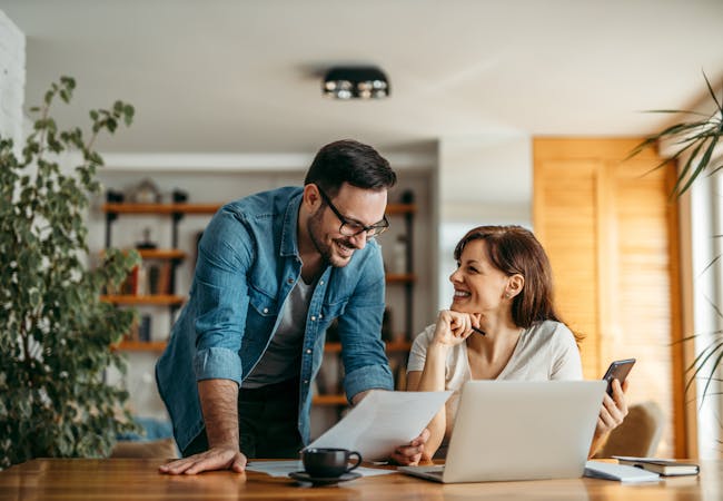 A smiling couple look at documents together while at home.
