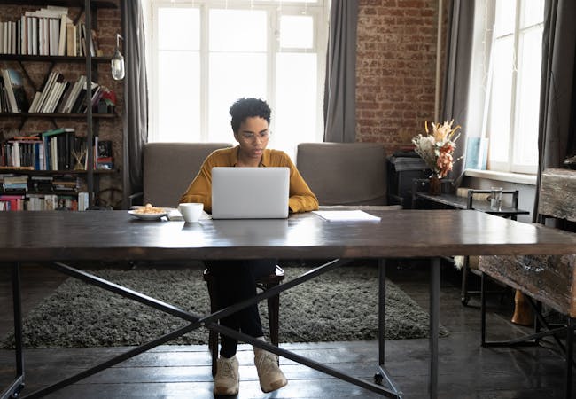 A person sits at a table in their home on a laptop computer.
