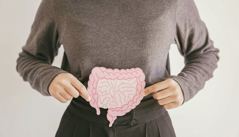 A woman from the shoulders down holds an illustration of the intestines over her stomach.