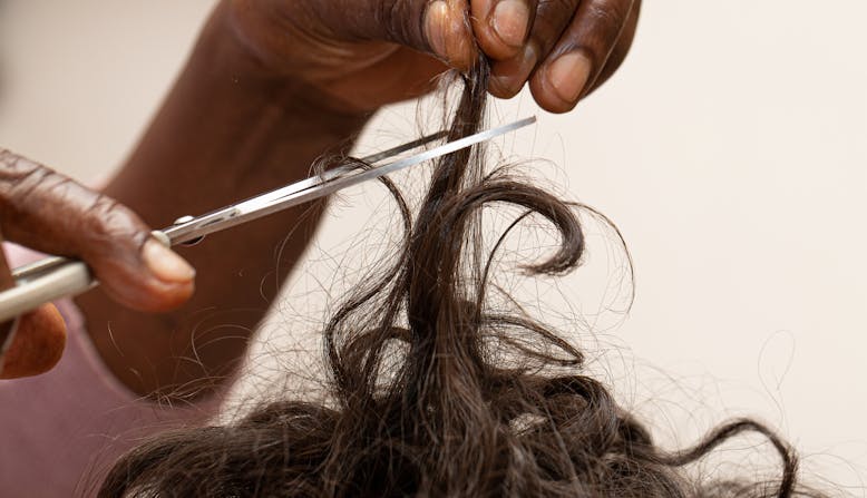 A black person cutting curly hair.