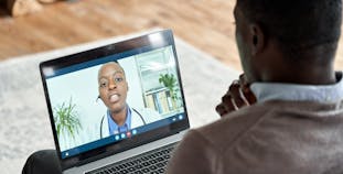 A Black man sits talking to a doctor on his laptop using telemedicine.