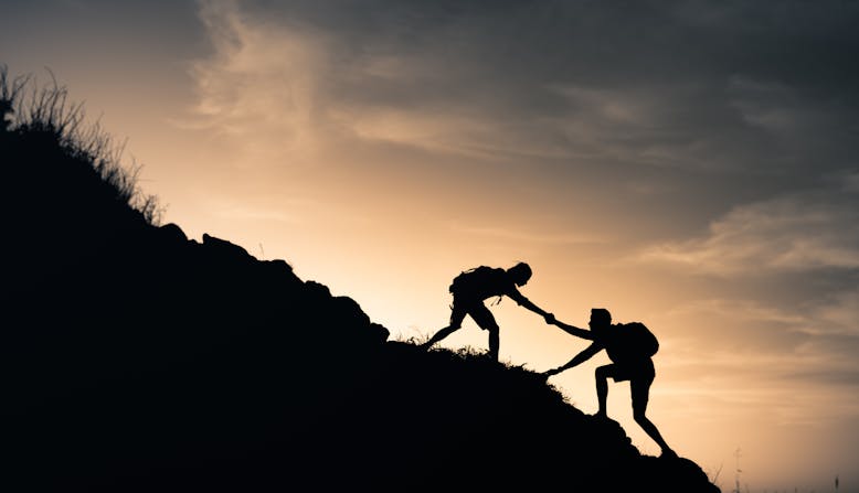 A hiker helping a friend climb a mountain