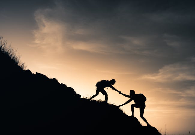 A hiker helping a friend climb a mountain