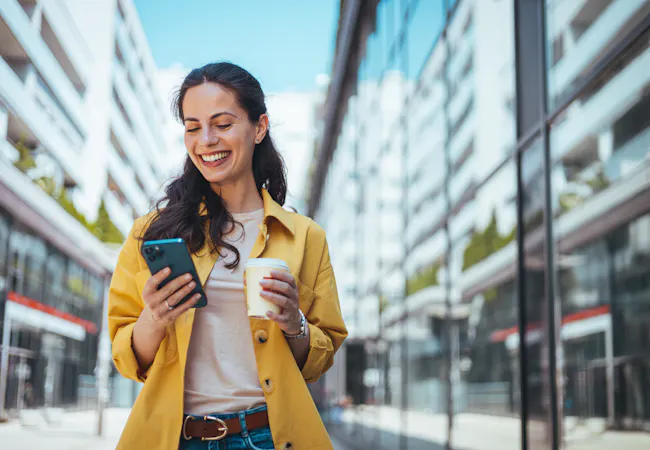 women smiling looking at her phone holding a coffee