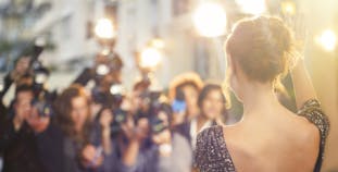 A famous woman shown from behind getting her photo taken by a crowd of photographers.