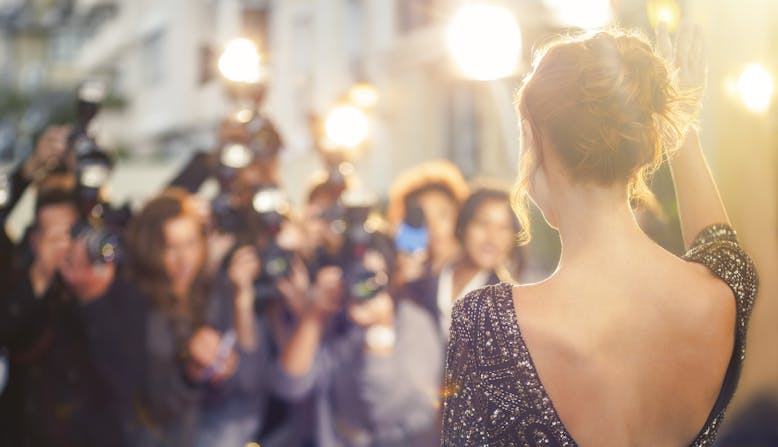 A famous woman shown from behind getting her photo taken by a crowd of photographers.