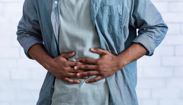 Shown from the neck down, a man holds his stomach in pain.