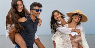 A mother and father give their two daughters piggyback rides on the beach.