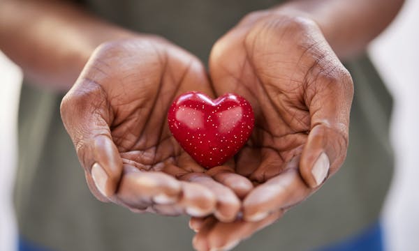A person is holding their hands out together, cupping a small heart-shaped object.