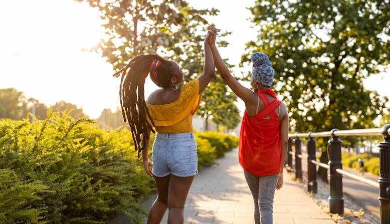 Two black women shown from behind as they high-five on a path outside.